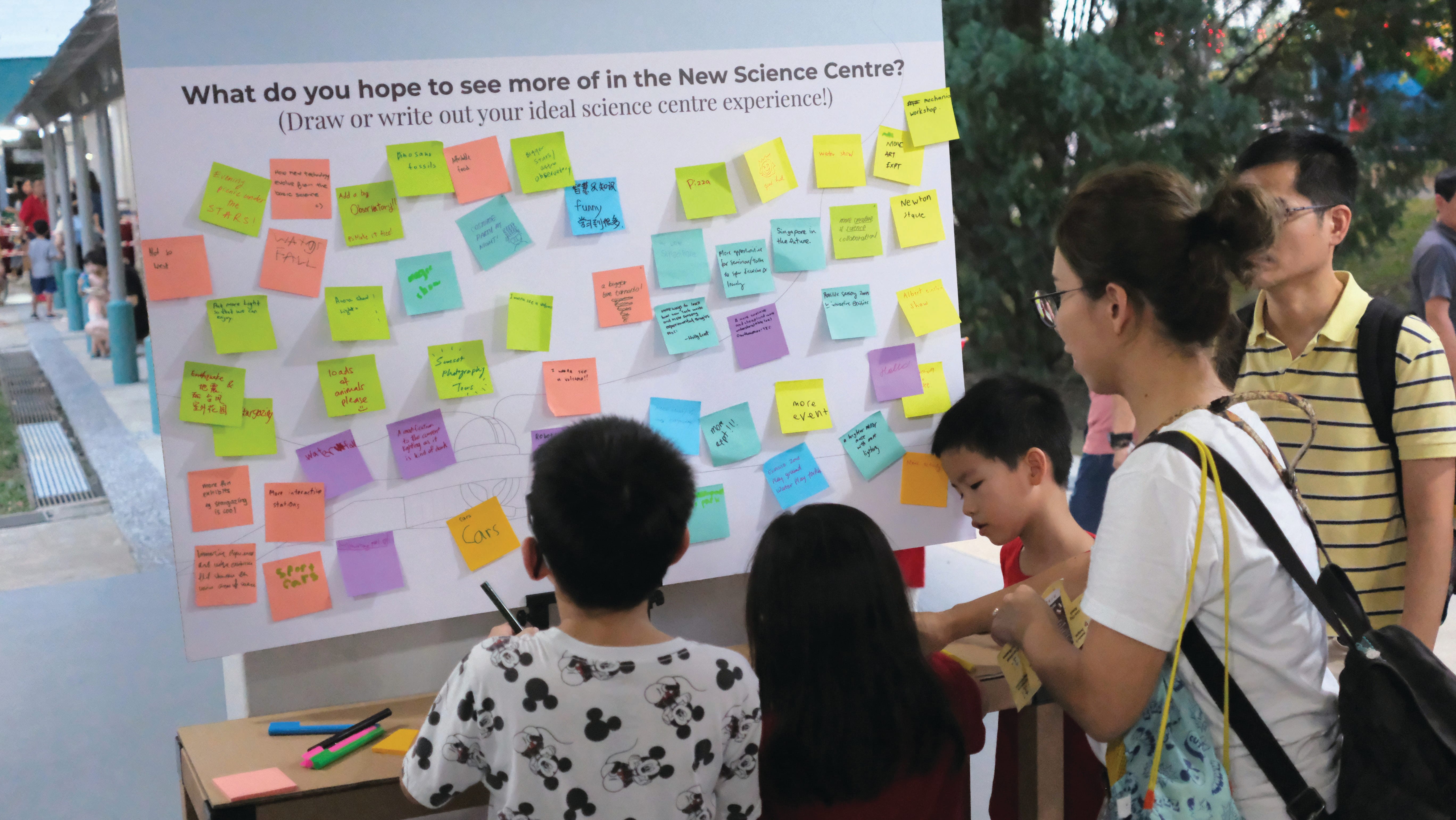 People participate in a survey about a future Science Centre. The survey question is displayed on a board covered with sticky notes with handwritten responses.